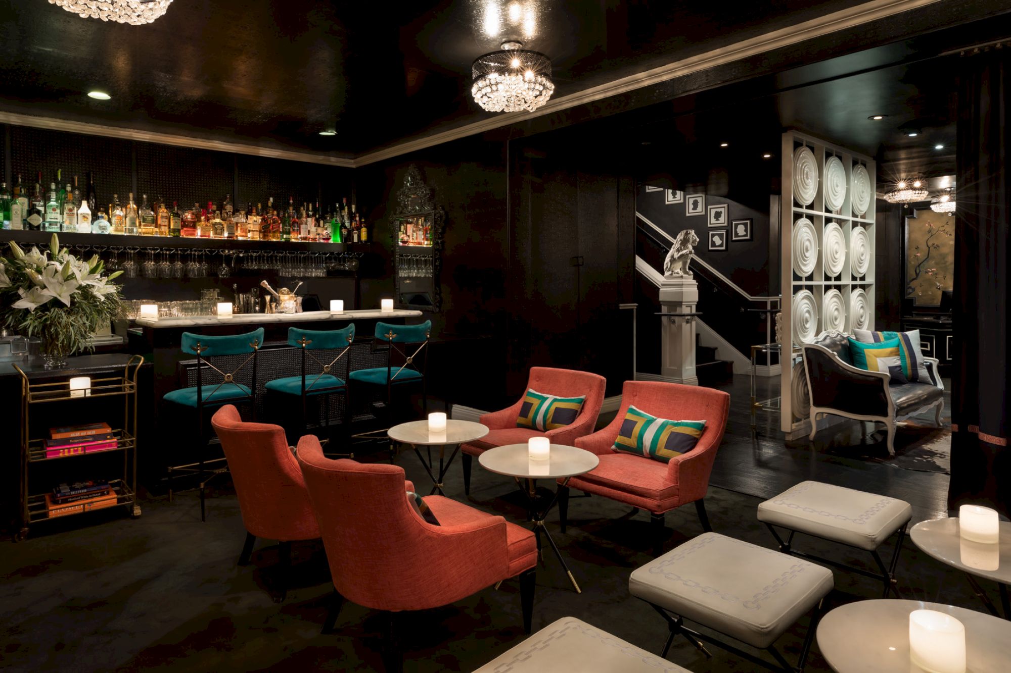 A cozy lounge bar with red chairs, teal barstools, and soft lighting; bottles and glasses lined up on the shelves.