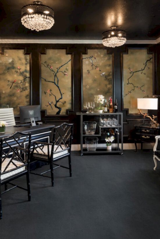 A stylish room with a dark interior, featuring a desk, chairs, decorative wall panels, chandeliers, and a bar cart with glasses.