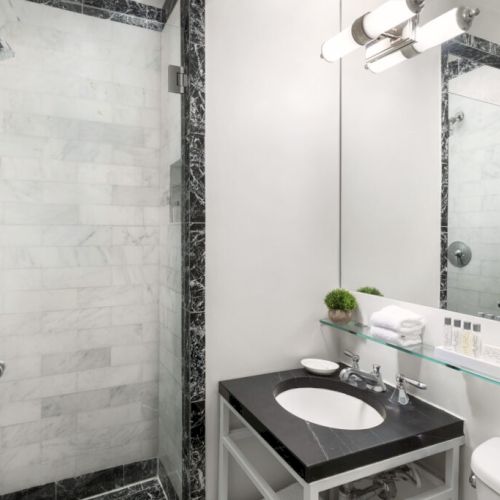 A modern bathroom with a glass shower, black vanity with a sink, white walls, and a large mirror.