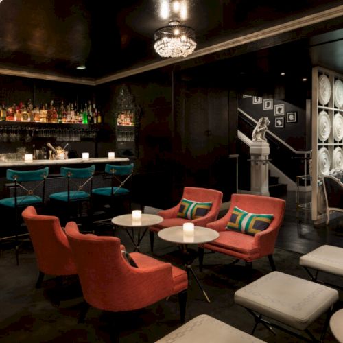 A stylish lounge with a fully stocked bar, red chairs, white tables, and ambient lighting, creating a cozy and elegant atmosphere.