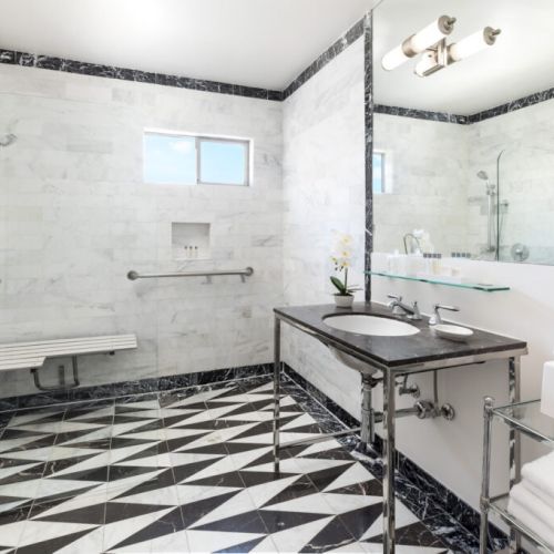 This image shows a modern bathroom with a marble design, featuring a walk-in shower, a sink, and a towel shelf, all in a sleek style.