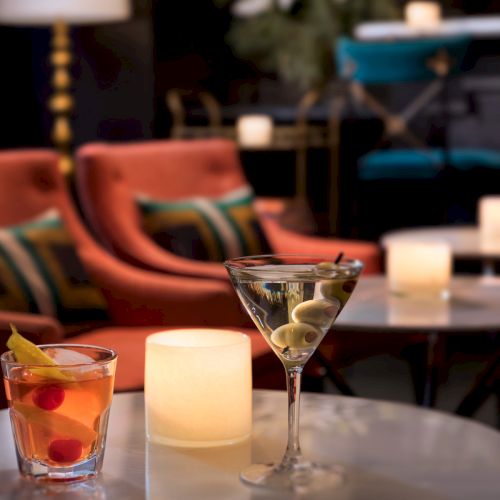 A cozy bar setting with cocktails on a table, surrounded by cushioned chairs and soft candlelight ambiance.