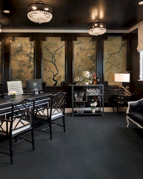 A sophisticated office with black decor, ornate chandeliers, a floral mural, and elegant furniture, including a bar cart and leather couch.