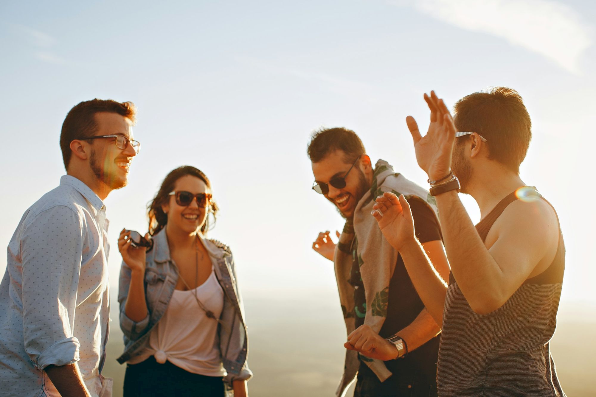 A group of four people enjoying themselves outdoors, smiling and engaged in conversation under a clear sky.